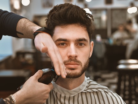 The hands of young barber making haircut to attractive man in barbershopの写真素材