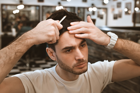 Working process in modern barbershop. Handsome hairdresser serving customer, styling hair for male client using hairdryer.の写真素材