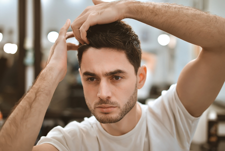 Man's body care. Self-styling hair. A beautiful boy with a beard makes his own hair.の写真素材