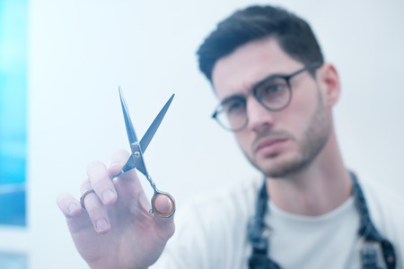 Barber keeps the scissors on his elongated hands against the background of a white wall. Focus on tools.の写真素材