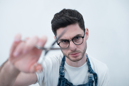 Barber keeps the scissors on his elongated hands against the background of a white wall.の写真素材