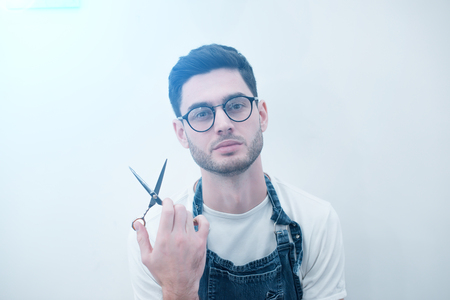 Barber keeps the scissors on his elongated hands against the background of a white wall.の写真素材