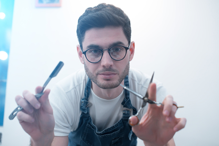 Barber keeps scissors and a razor against the background of a white wall.の写真素材