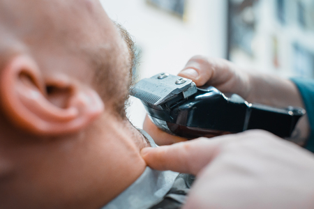 Barber leveled his beard to the client machine for shaving. The client gets the perfect shape of your beard. Soft focus.の写真素材