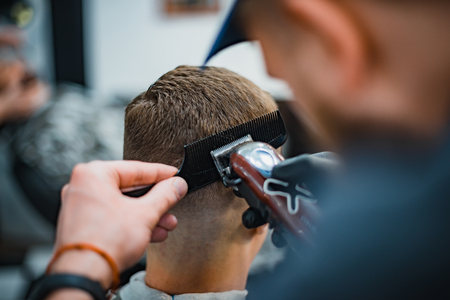 Man gets a cool haircut in barbershop. Barber makes the cut man electric razor. Men's care head. Soft focus.の写真素材
