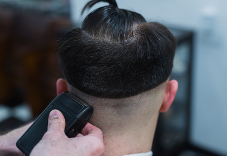 The hands of young barber making haircut to attractive man in barbershopの写真素材