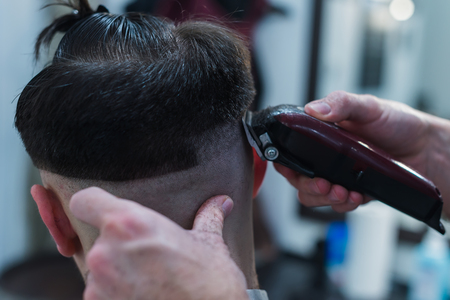 The hands of young barber making haircut to attractive man in barbershopの写真素材
