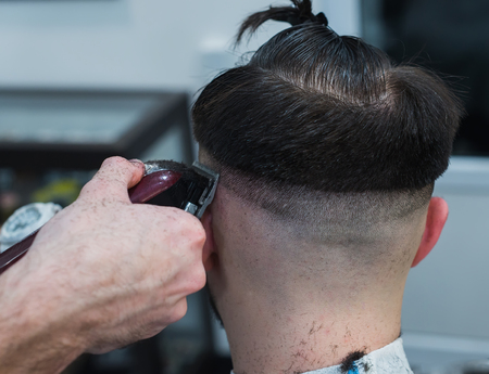 The hands of young barber making haircut to attractive man in barbershopの写真素材