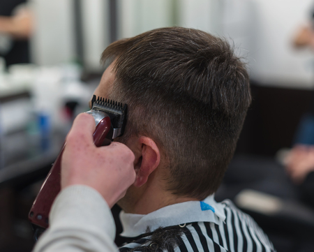 The hands of young barber making haircut to attractive man in barbershopの写真素材