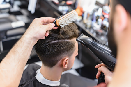 Professional barber styling hair of his client. Barber makes hair styling with a hair dryer.の写真素材