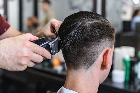 Interior shot of working process in barbershop. Side view of handsome young man getting trendy beard haircut in modern barbershop. Cool male hairstylists serving clientsの写真素材