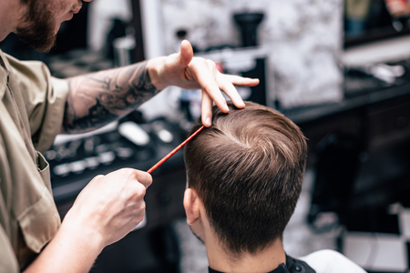 The hands of young barber making haircut to attractive man in barbershopの写真素材