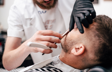 Shave beards in barbercos. Men's haircut and facial care. Barber makes a haircut to the client.の写真素材