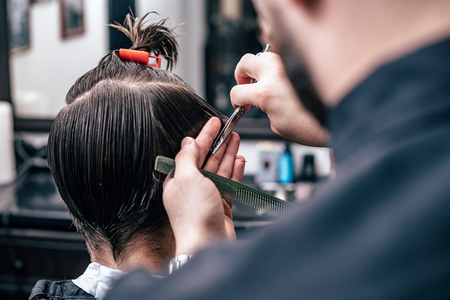 The hands of young barber making haircut to attractive man in barbershopの写真素材