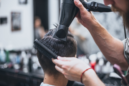 Getting perfect shape. Close-up side view of young bearded man getting beard haircut by hairdresser at barbershopの写真素材