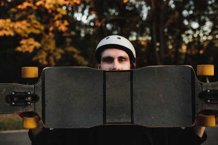 Charismatic guy in a white helmet holds a longboard.の写真素材