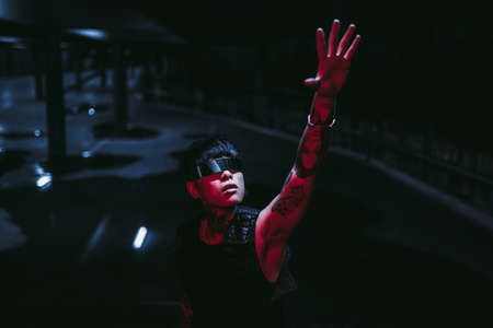 Cyberpunk. Tattooed man in futuristic glasses pulls his arm. The concept of the future of mankind.の写真素材
