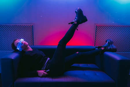 Futuristic fashion style. A woman in neon glasses lies on the couch with her leg raised.の写真素材