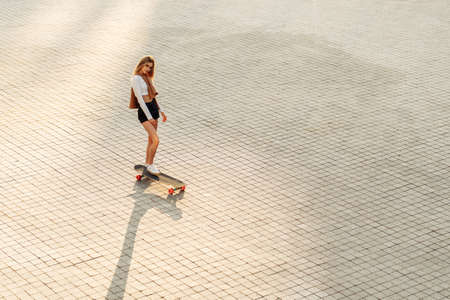 Young woman rides a longboard.