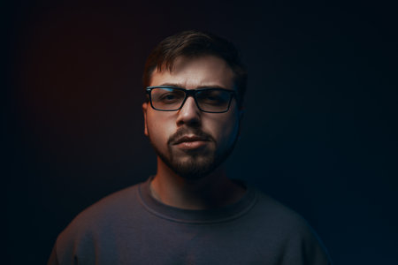 Portrait of a serious young man in glasses on a dark background.