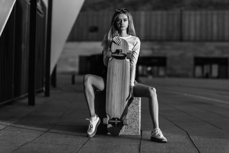 Cool young woman with a longboard sitting on the stairs in sunglasses. Casual styleの写真素材