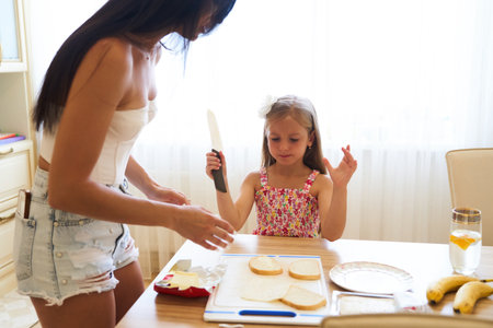 Mother and Daughter Preparing Sandwiches Together in Bright Kitchen During Afternoonの写真素材