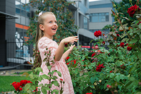 Young Girl Joyfully Interacting With Vibrant Red Roses in an Urban Garden During Daytimeの写真素材