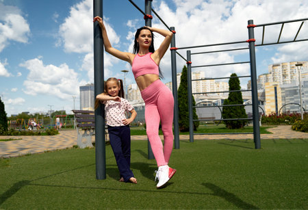 Mother and daughter in activewear exercising together at a park on a sunny day