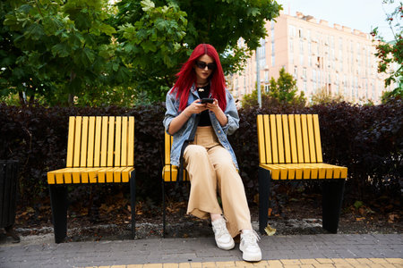 Young woman with red hair using smartphone while seated in a park