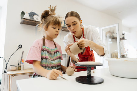 A woman teaches a child pottery in a bright studio during daytime activities