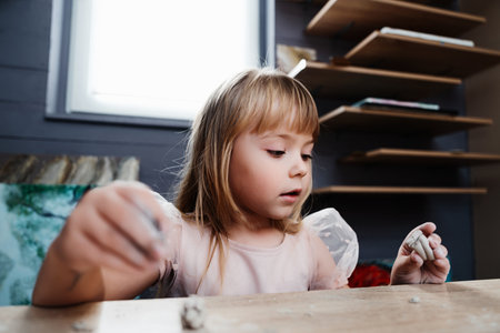 Girl engaged in creative clay modeling indoors at a cozy workspaceの写真素材