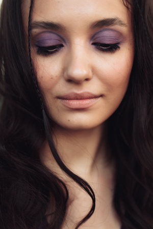 Charming portrait of a young woman with purple eyeshadow and long dark hairの写真素材