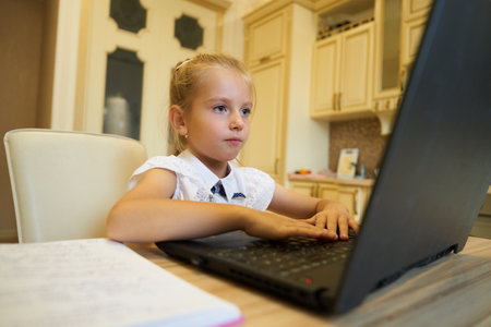 Young girl focused on her laptop while studying at a kitchen tableの写真素材