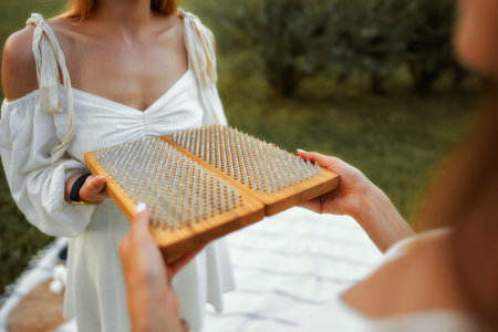 Person holding a wooden board with spikes during a wellness activity outdoors