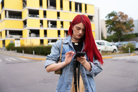 Young woman with red hair checks phone while walking through parking lot