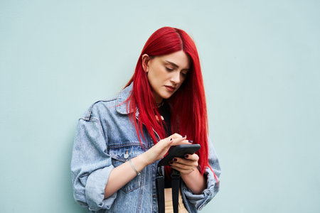 Young woman with red hair texting on her phone against a light blue wallの写真素材