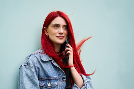 Young woman with vibrant red hair making a phone call outside in daylightの写真素材