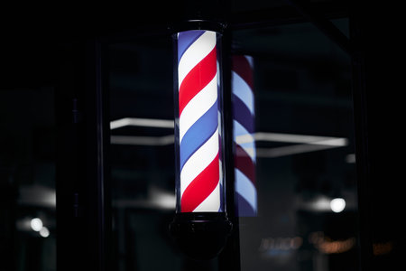Barber pole with red, white, and blue stripes illuminated at nightの写真素材