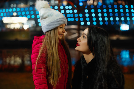 Smiling woman and girl enjoy a joyful moment together at a festive evening event by the waterの写真素材
