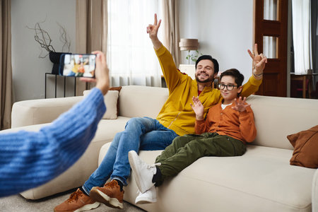 Father and son making peace signs while posing on a couch indoorsの写真素材