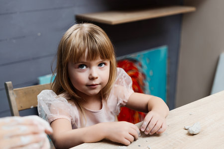 Girl with blonde hair sitting at a wooden table in an artistic space