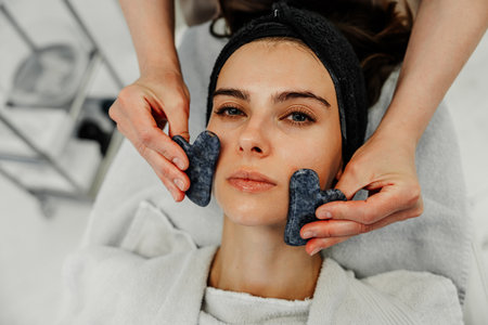 Woman receiving facial treatment with gua sha tools at spa during late morning in calm atmosphereの写真素材