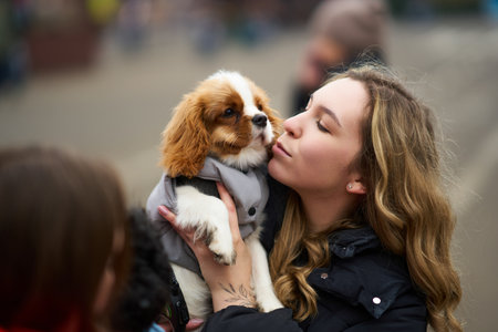 Woman shares a warm moment with a small dog outdoors in a bustling city environment during a cool dayの写真素材