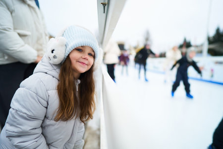 Person watches ice skaters at outdoor rink during winter dayの写真素材