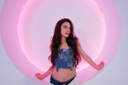 Young woman poses playfully in front of a glowing round light installationの写真素材