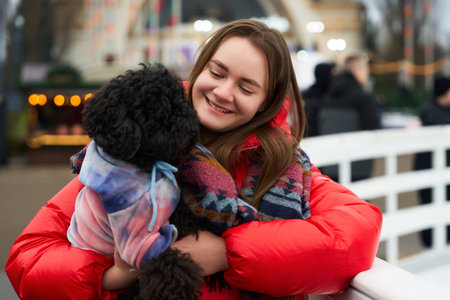 Young woman smiles while holding a small dog at a festive outdoor market in winterの写真素材
