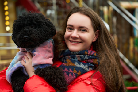 Woman happily holds black dog while smiling at a playground during a chilly day