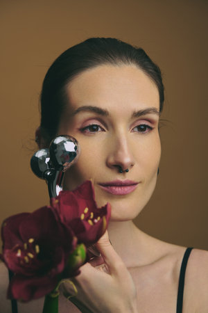 Woman using a facial massager with flowers in a studio settingの写真素材