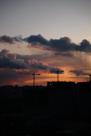 Construction cranes silhouetted against a colorful sunset in the cityの写真素材