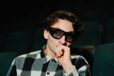 Young man wearing glasses enjoys a film in a dark theaterの写真素材